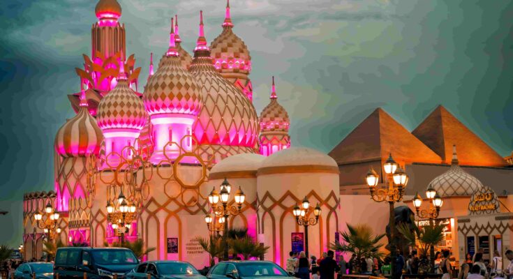 Global Village Dubai at night with pink and gold illuminated domes, Egyptian pyramids, and street lamps — GlanceAsia Travel Guide