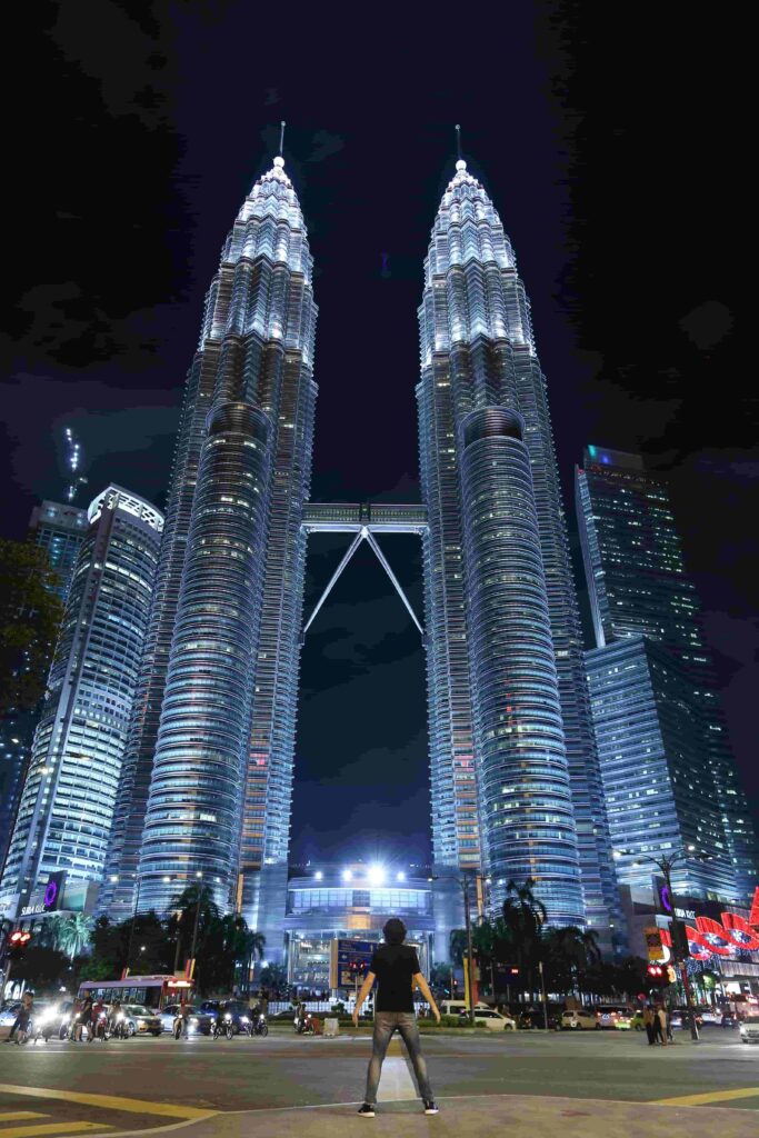 Traveller standing in front of the illuminated Petronas Twin Towers at night in Kuala Lumpur Malaysia