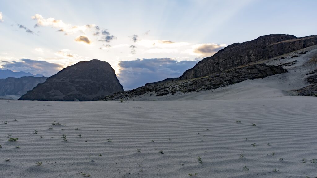 Scenic view of Sarfaranga Cold Desert in Skardu with sand dunes and mountains under a cloudy sky.