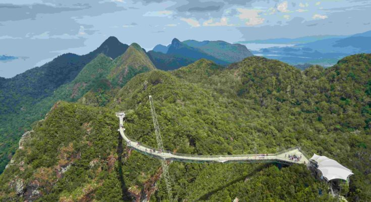 Aerial view of Langkawi Sky Bridge curving across mountain ridge with surrounding green rainforest mountains and Andaman Sea in background Malaysia
