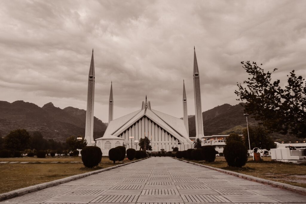 Faisal Mosque Islamabad Pakistan with four minarets and Margalla Hills in background under cloudy sky