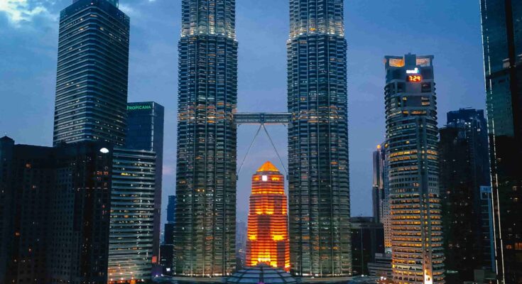 Aerial view of Petronas Twin Towers and Kuala Lumpur skyline at blue hour with city lights glowing