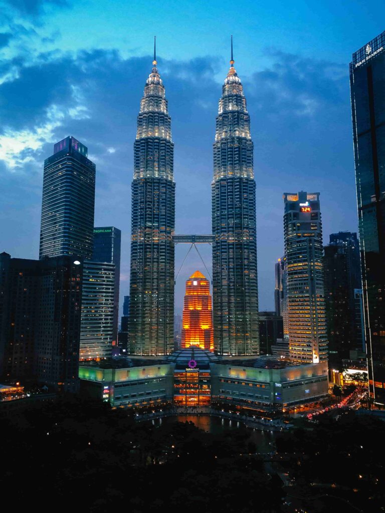 Aerial view of Petronas Twin Towers and Kuala Lumpur skyline at blue hour with city lights glowing. The Malaysia 7 Days Budget Travel Plan