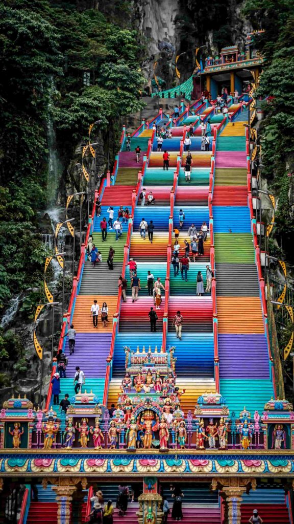 Colourful rainbow stairs leading up to Batu Caves temple in Kuala Lumpur Malaysia with Hindu statues and jungle waterfall