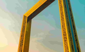 The Dubai Frame photographed from below at golden hour, its gold-latticed towers rising against a teal and amber sky with palm trees in the foreground, Dubai, UAE