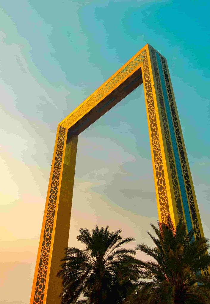 The Dubai Frame photographed from below at golden hour, its gold-latticed towers rising against a teal and amber sky with palm trees in the foreground, Dubai, UAE
