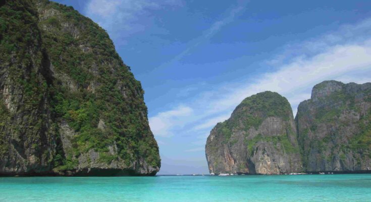 The iconic entrance of Maya Bay featuring clear blue skies and vibrant neon-turquoise water in Southern Thailand