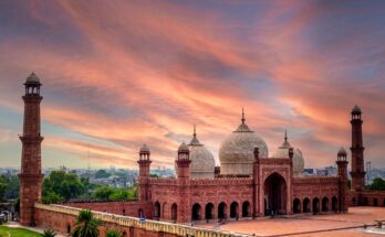 Majestic panoramic view of Badshahi Mosque Lahore at sunset, showcasing its red sandstone structure and white marble domes under a vibrant orange sky.