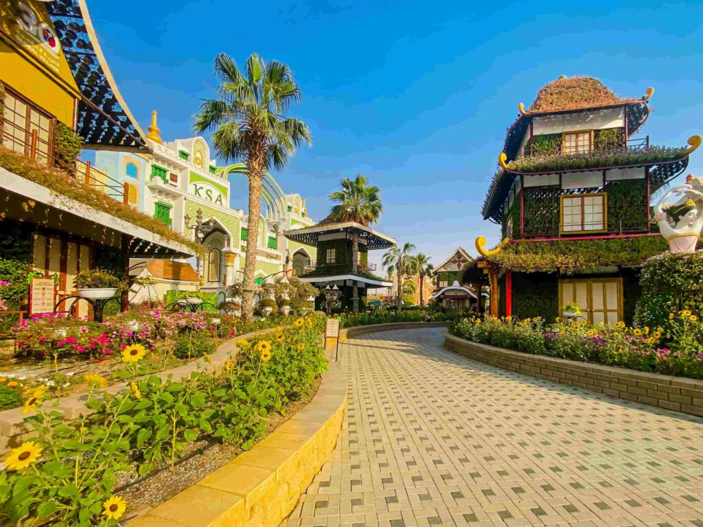 Colourful KSA and Asian pavilions with sunflowers and palm trees at Global Village Dubai during daytime — GlanceAsia Travel Blog