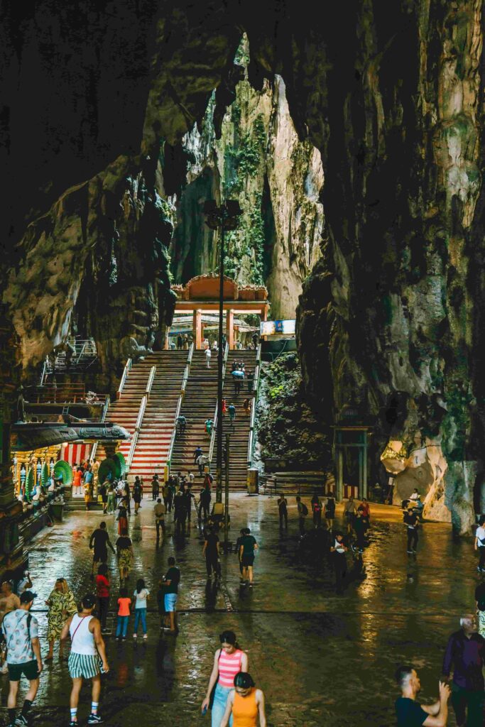 Inside Cathedral Cave at Batu Caves Kuala Lumpur showing massive limestone ceiling with sunlight streaming through and visitors exploring below
