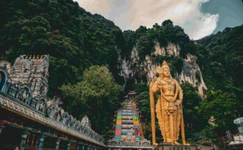 Golden Lord Murugan statue standing in front of rainbow stairs and limestone cliffs at Batu Caves Kuala Lumpur Malaysia