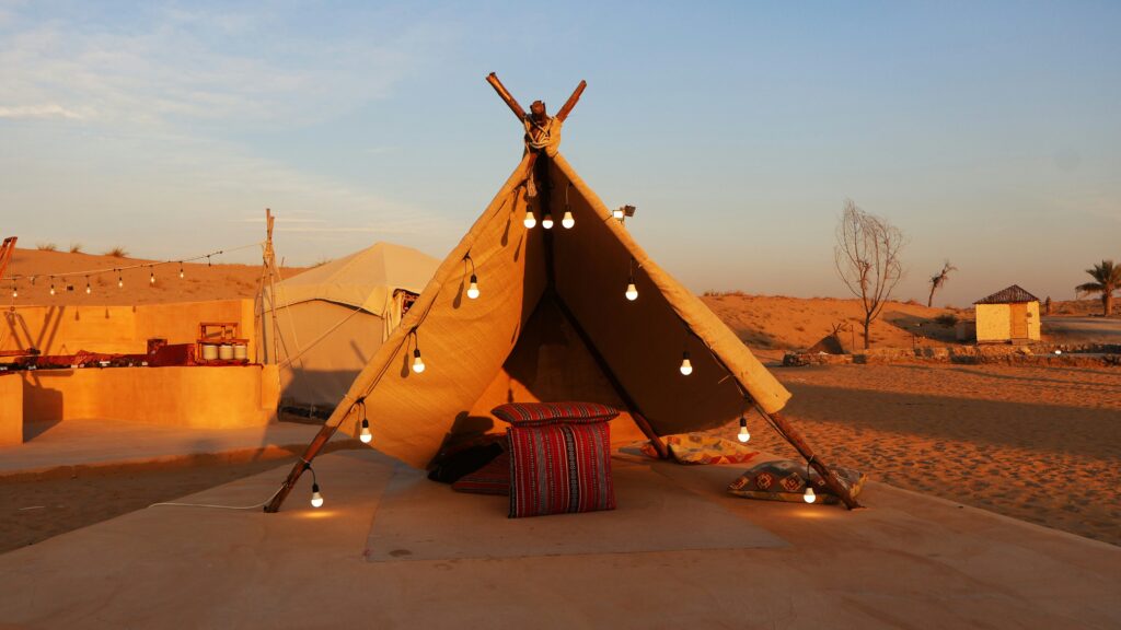 Cozy Bedouin camp setup in the Dubai desert at sunset with hanging lights and cushions."