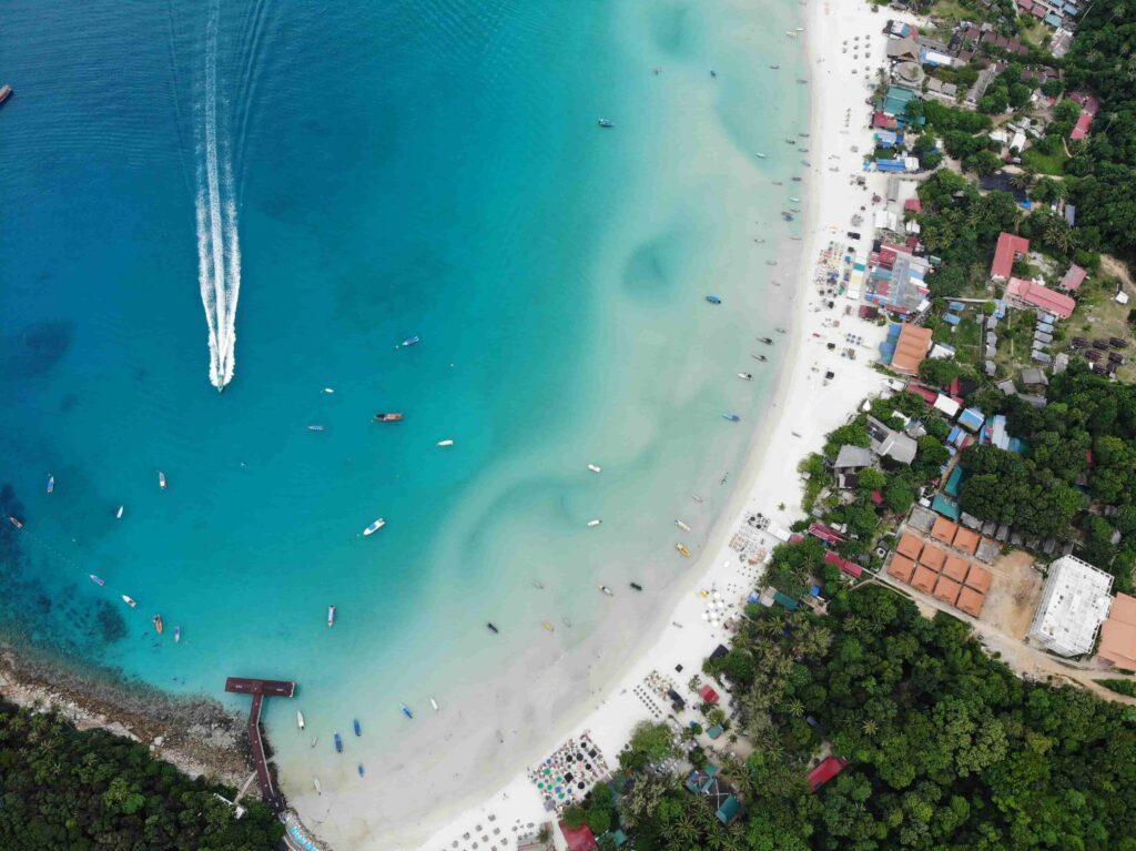 Aerial view of Long Beach on Perhentian Kecil, Malaysia, showing turquoise waters, white sand, and traditional boats anchored along the shore. Perhentian Islands