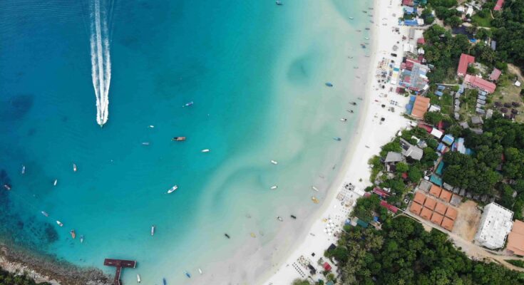 Aerial view of Long Beach on Perhentian Kecil, Malaysia, showing turquoise waters, white sand, and traditional boats anchored along the shore. Perhentian Islands