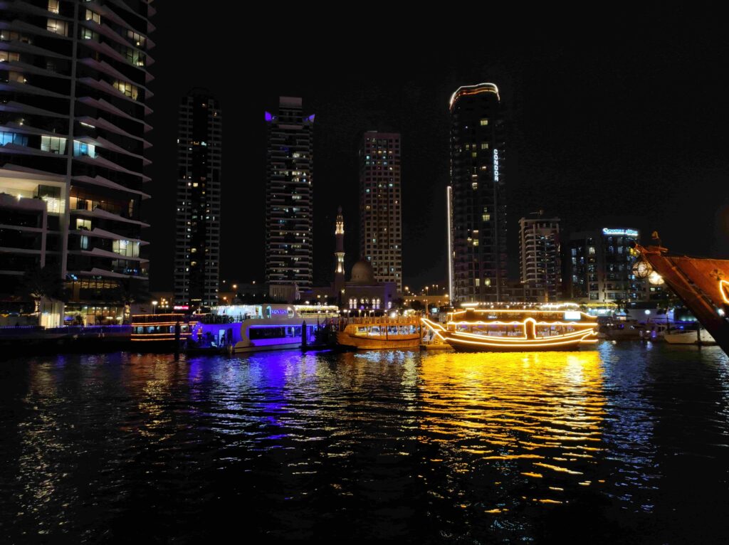Illuminated mosque and dhow boats along Dubai Marina waterfront at night