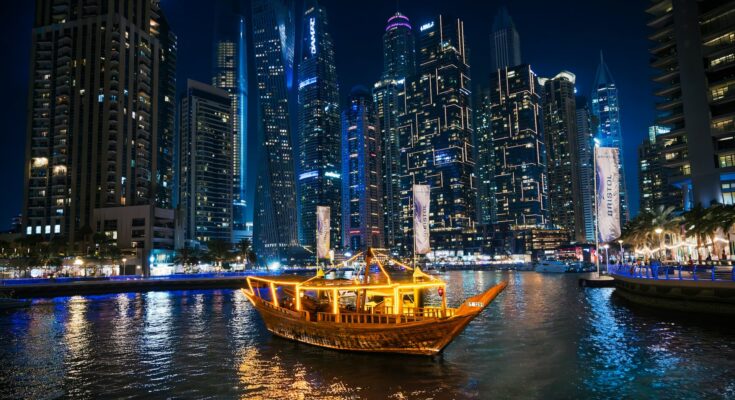 Traditional dhow cruise boat lit up at night in front of Dubai Marina skyscrapers
