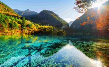 Sunlight streaming through autumn leaves over a turquoise lake in Jiuzhaigou Valley, Sichuan, China