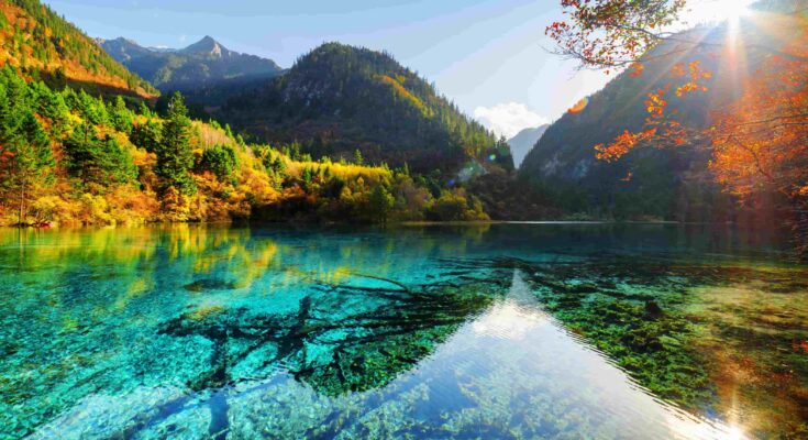 Sunlight streaming through autumn leaves over a turquoise lake in Jiuzhaigou Valley, Sichuan, China