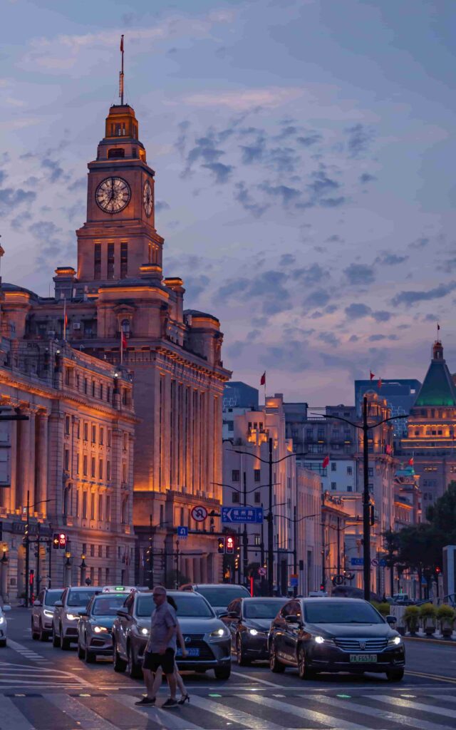 Pedestrians crossing near the Bund Shanghai's clock tower at dusk with city traffic