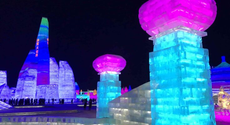 Illuminated ice towers glowing pink and blue at Harbin Ice and Snow World at night